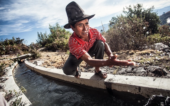  Un uomo accovacciato accanto a un canale di irrigazione.