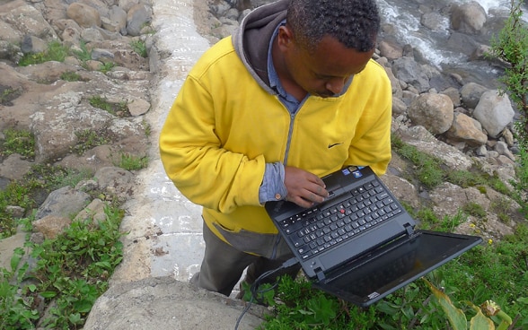  Un uomo in piedi vicino a un fiume lavora su un computer portatile.