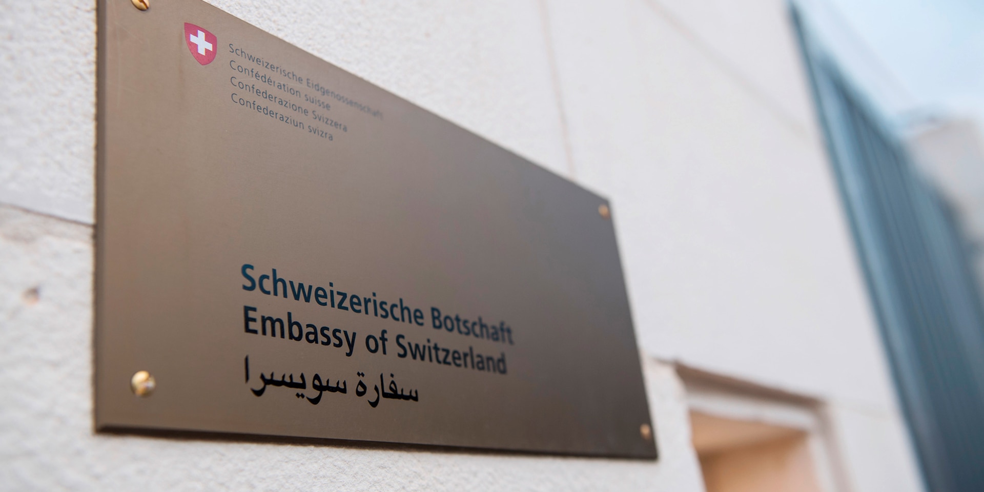 Écriteau sur lequel figure l’inscription «Ambassade de Suisse» en allemand, anglais et arabe.