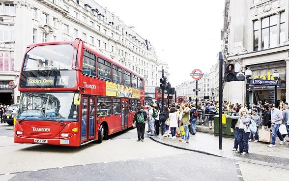 Double decker bus passes the famous Oxford Circus in London, people waiting at the roadside.