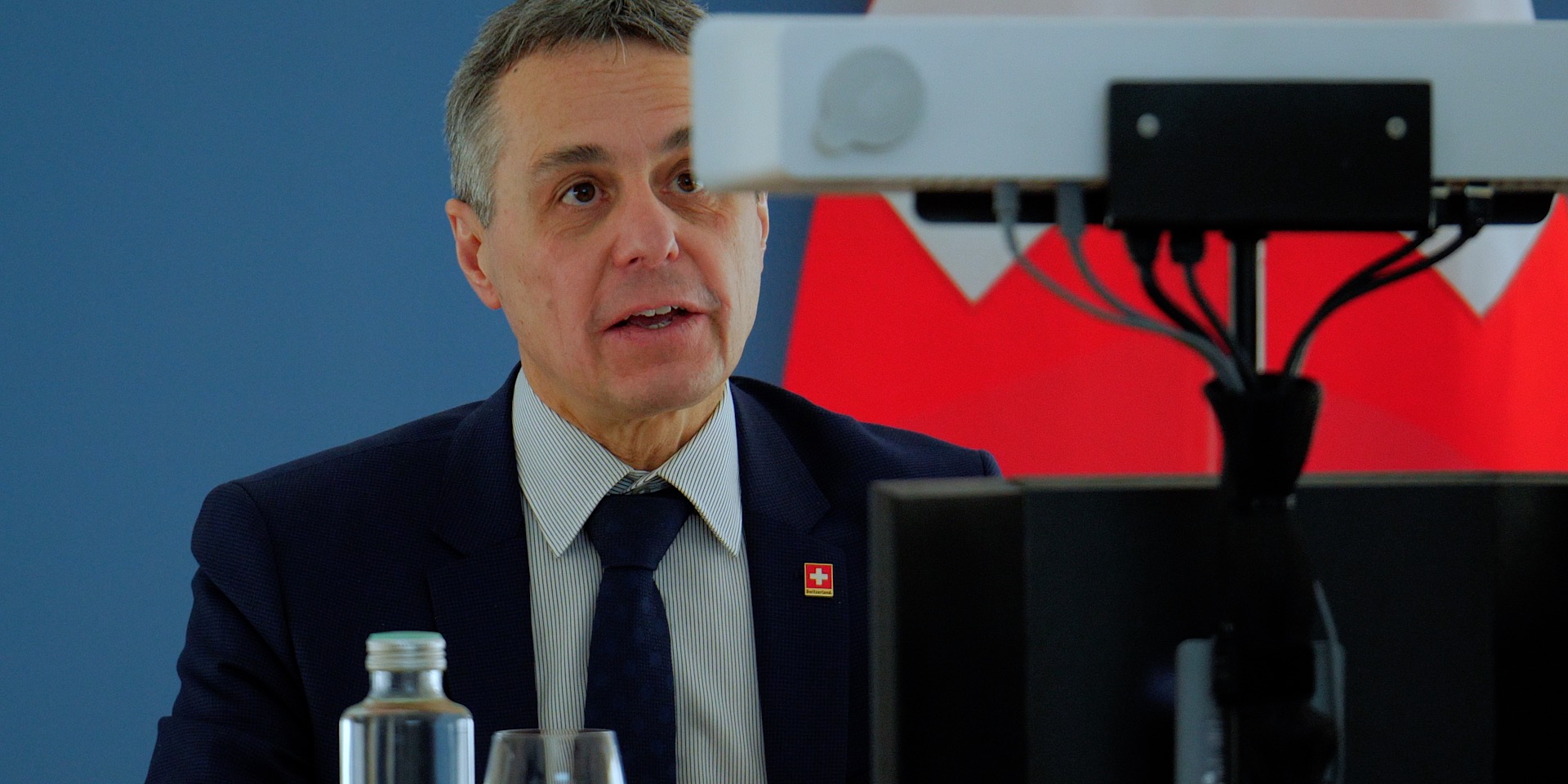 Le conseiller fédéral Ignazio Cassis prononce un discours face à une caméra lors d’une conférence virtuelle. Derrière lui, le drapeau de la Suisse.