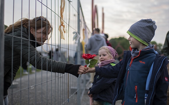 Eine Frau reicht durch den wegen der Pandemie errichteten Grenzzaun in Konstanz zwei Kindern eine Blume.