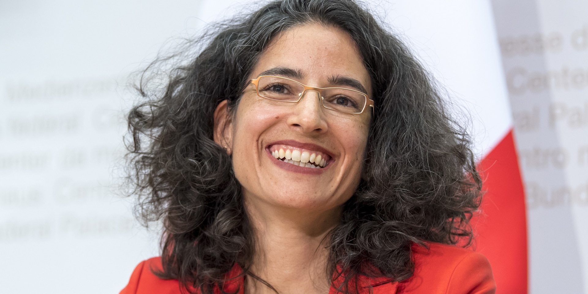 Portrait de Corinne Cicéron Bühler, souriante avec, en arrière-plan, le drapeau de la Suisse.