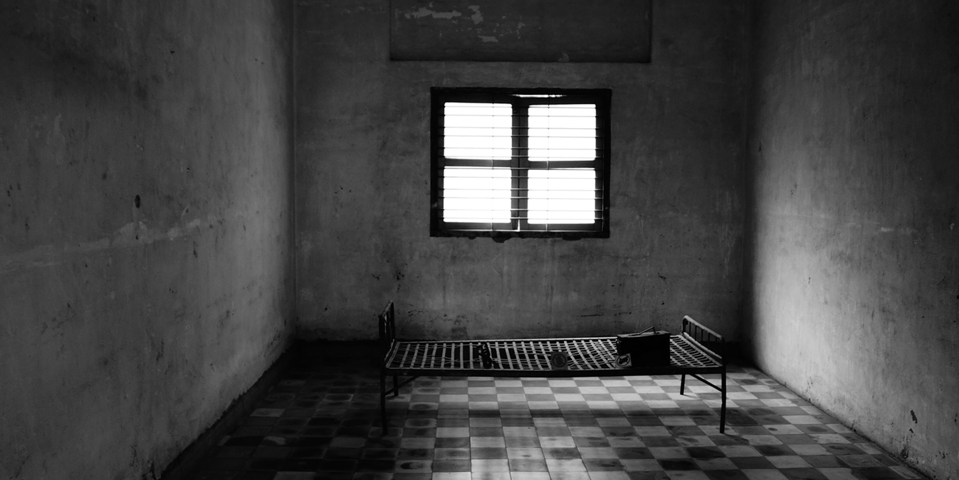 L'image montre une cellule avec une fenêtre et un cadre de lit en noir et blanc.
