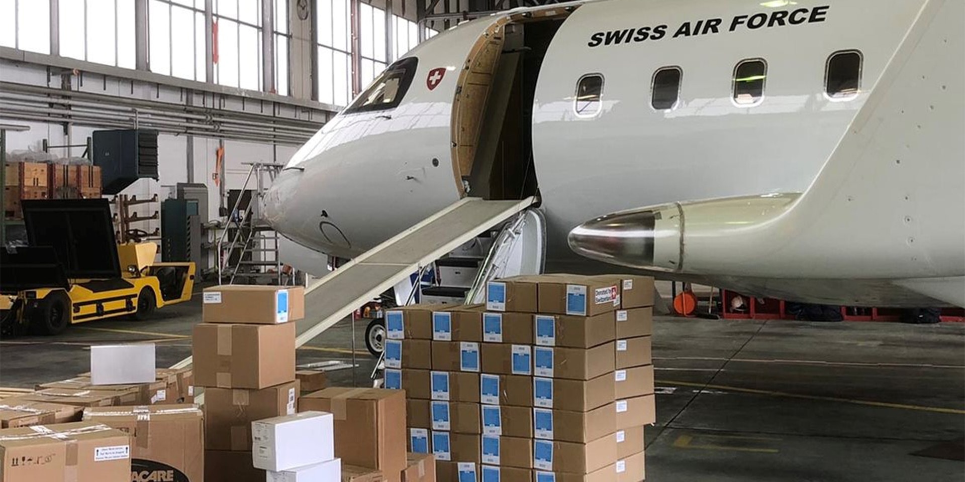 Sur l'image, on voit un avion de la Confédération suisse dans le hangar. Devant elle, des boîtes contenant du matériel de secours.