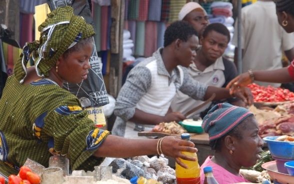 Eine Frau greift auf einem Marktstand in Afrika nach einer Flasche, um sie zu verkaufen.