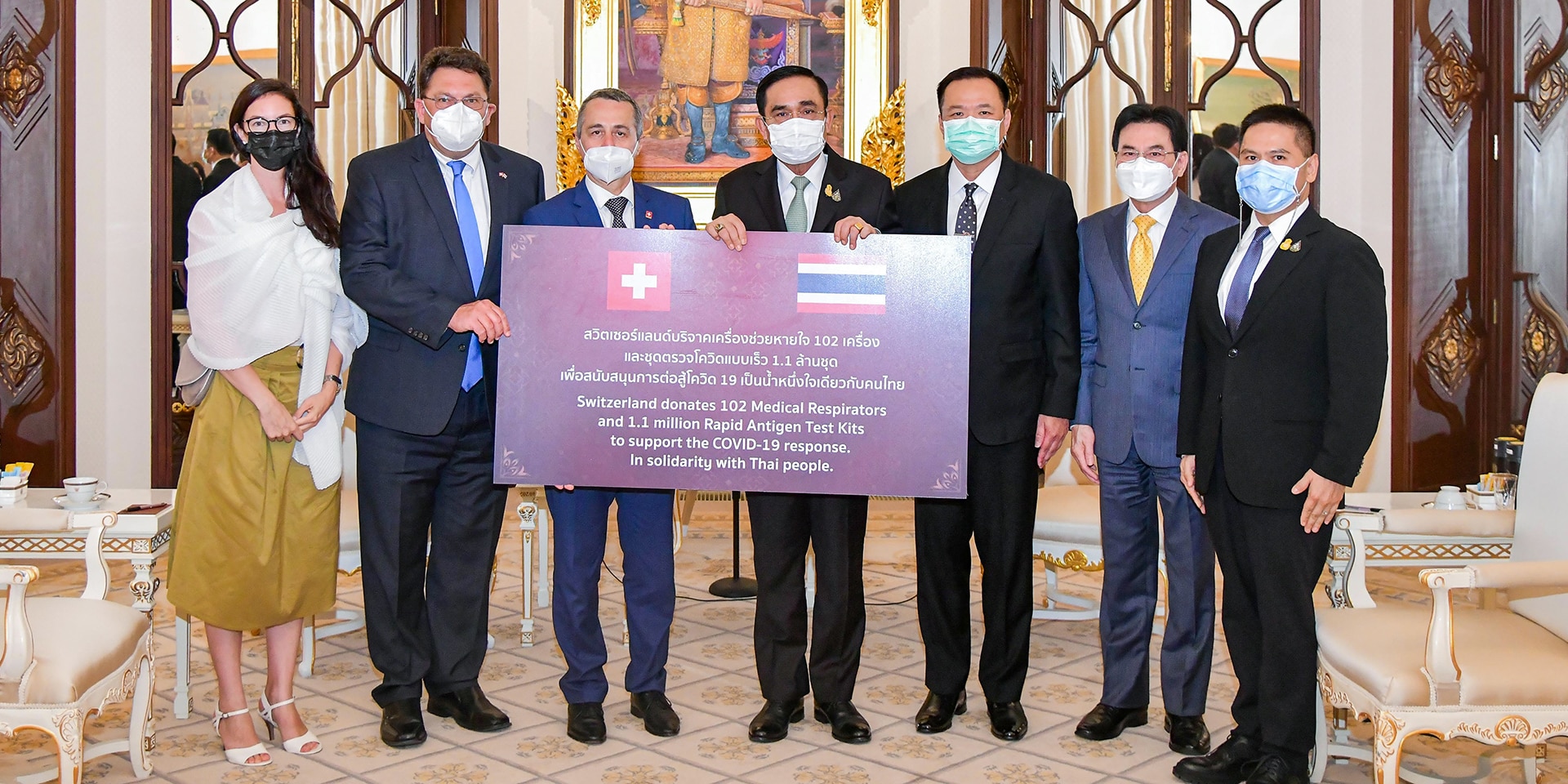 Various people stand in a room in front of a sign describing Switzerland's aid delivery.