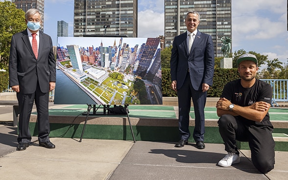 Bundesrat Ignazio Cassis (stehend in der Mitte) überreicht UNO-Generalsekretär António Guterres (linksstehend) im Beisein des Künstlers Saype (rechts hauernd) ein Bild des riesigen Freskos das zwei Kinder zeigt, die ihre Welt von morgen zeichnen.