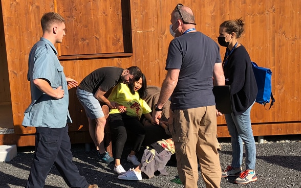 A pregnant woman is propped up against a wooden barrack and is bleeding.