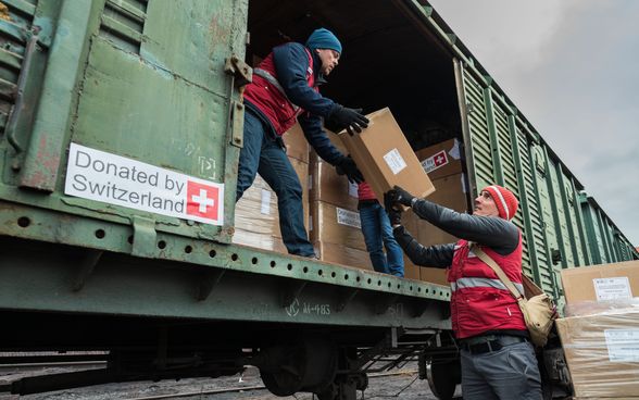 Men in red jackets stand at the open door of a goods wagon and load boxes.