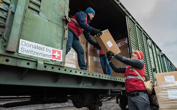 Del materiale diretto in Ucraina viene caricato da due persone su un vagone del treno che riporta la scritta "Donated by Switzerland".  