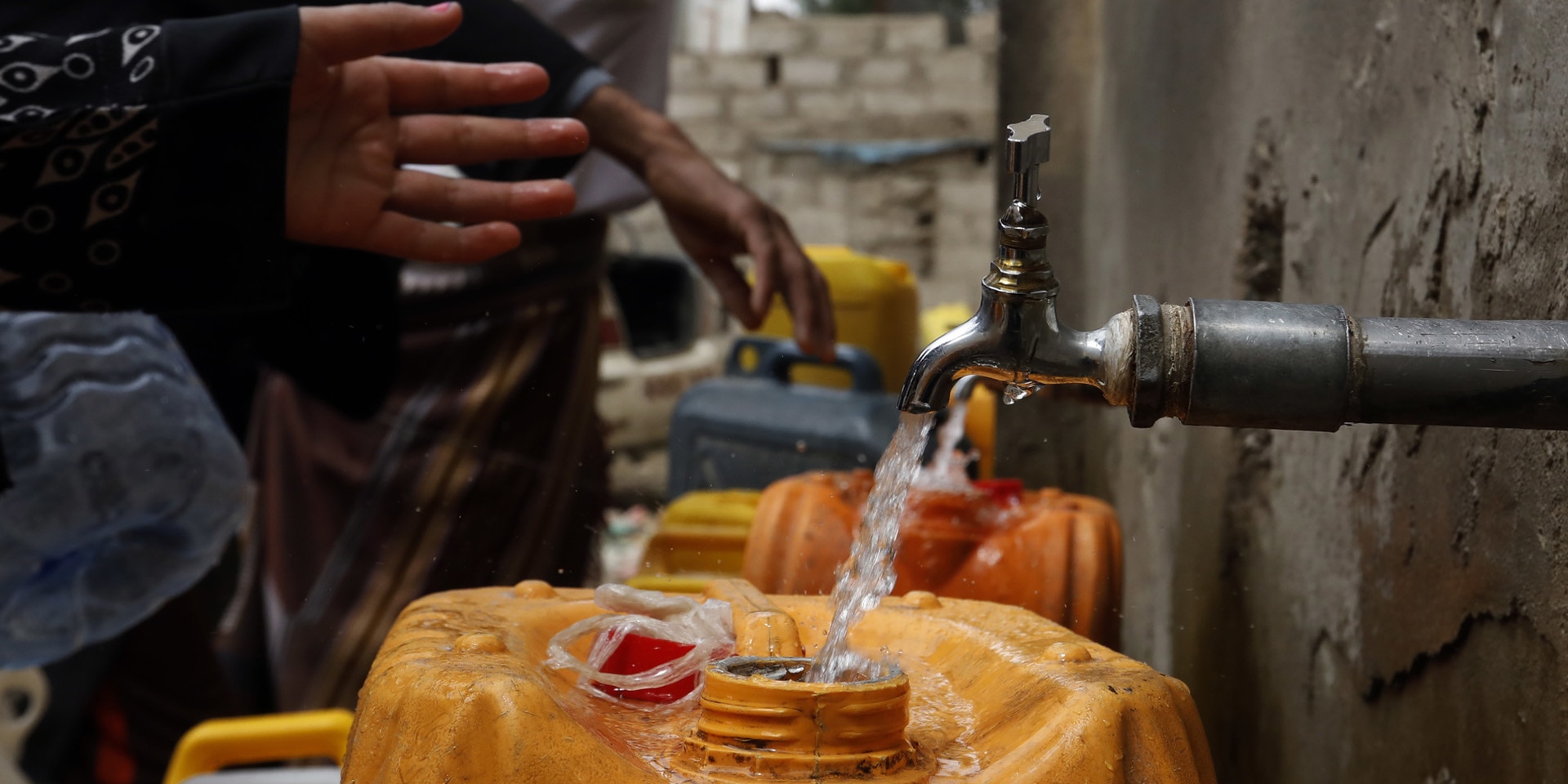 Clean water flows from a pipe into a yellow plastic canister.