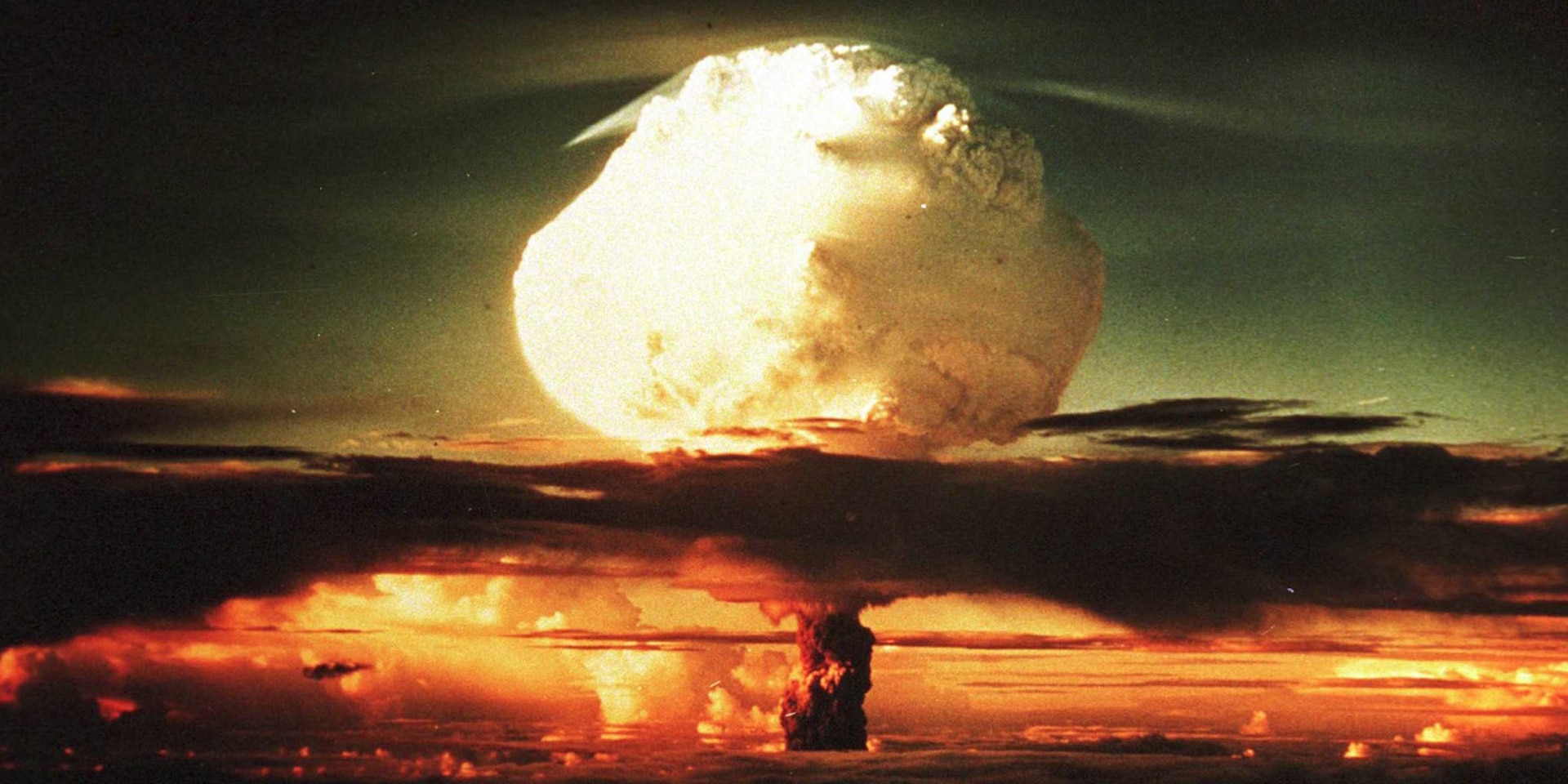A mushroom cloud following detonation of a nuclear bomb rises into the sky.
