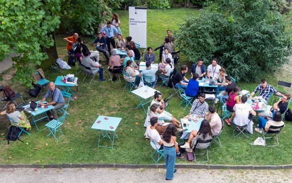 In a meadow, young people are sitting around tables talking.