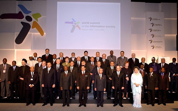 Representatives of various states pose in front of a poster of the World Summit on the Information Society in Geneva.