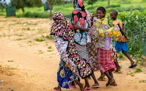 Ein afrikanische Frau und Kinder gehen einer staubigen Strasse entlang.