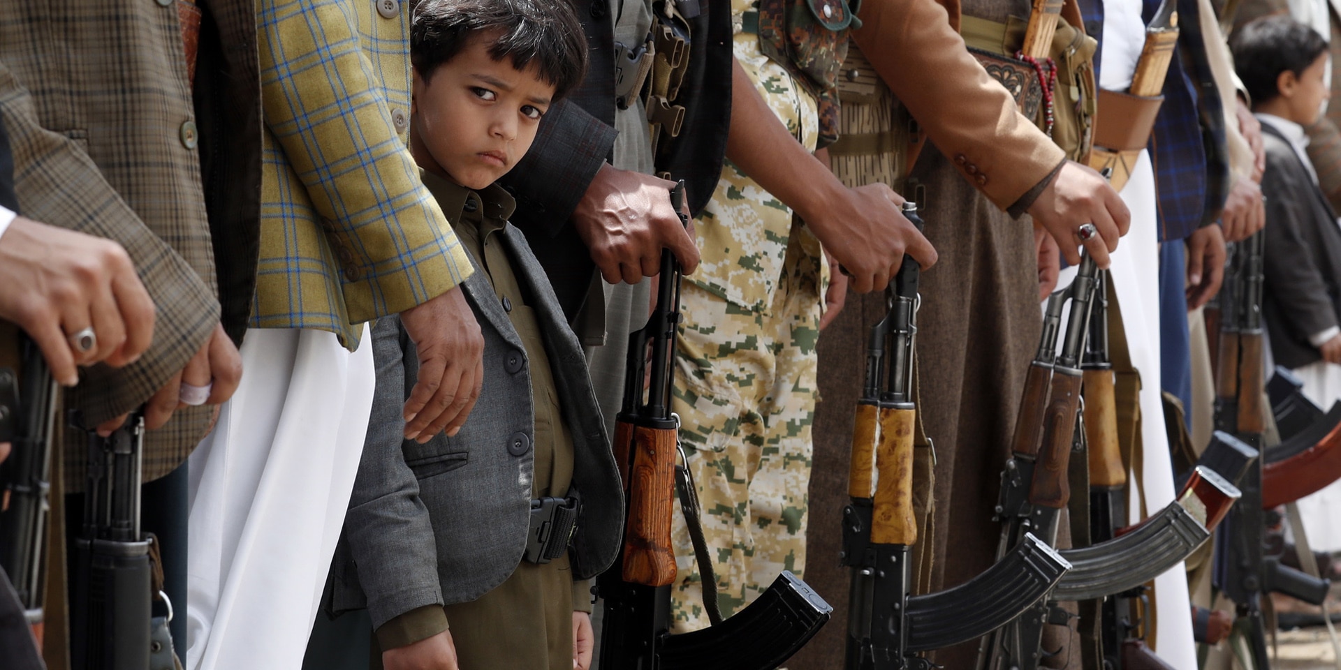 A Yemeni boy stands in a line of adults holding guns.