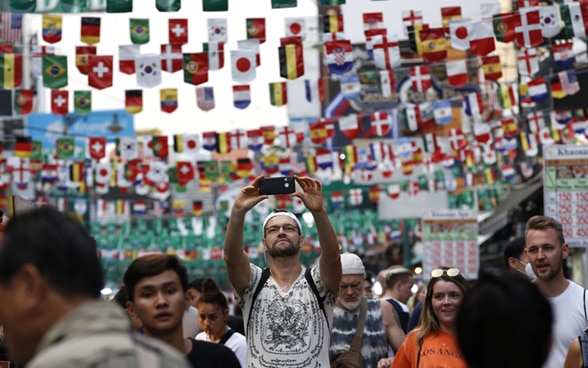 Un turista si scatta un selfie in una strada affollata con le bandiere appese in alto.