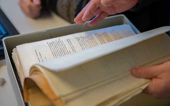 A person flips through documents in a box with his hands. 