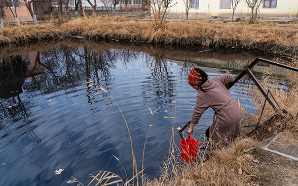 Une jeune fille qui porte un foulard rouge puise de l’eau avec un sceau.