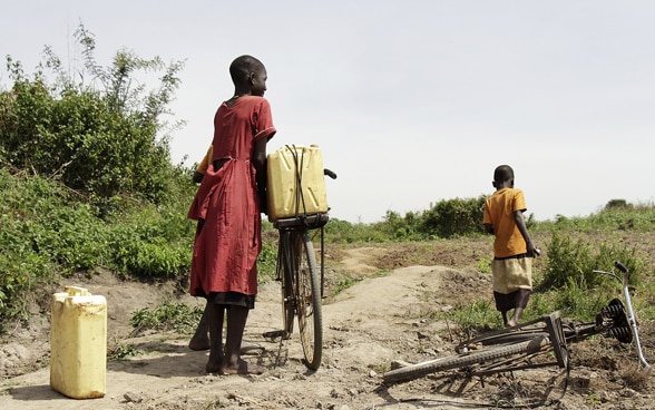 Deux enfants d’origine africaine transportent des bidons jaunes sur des vélos.