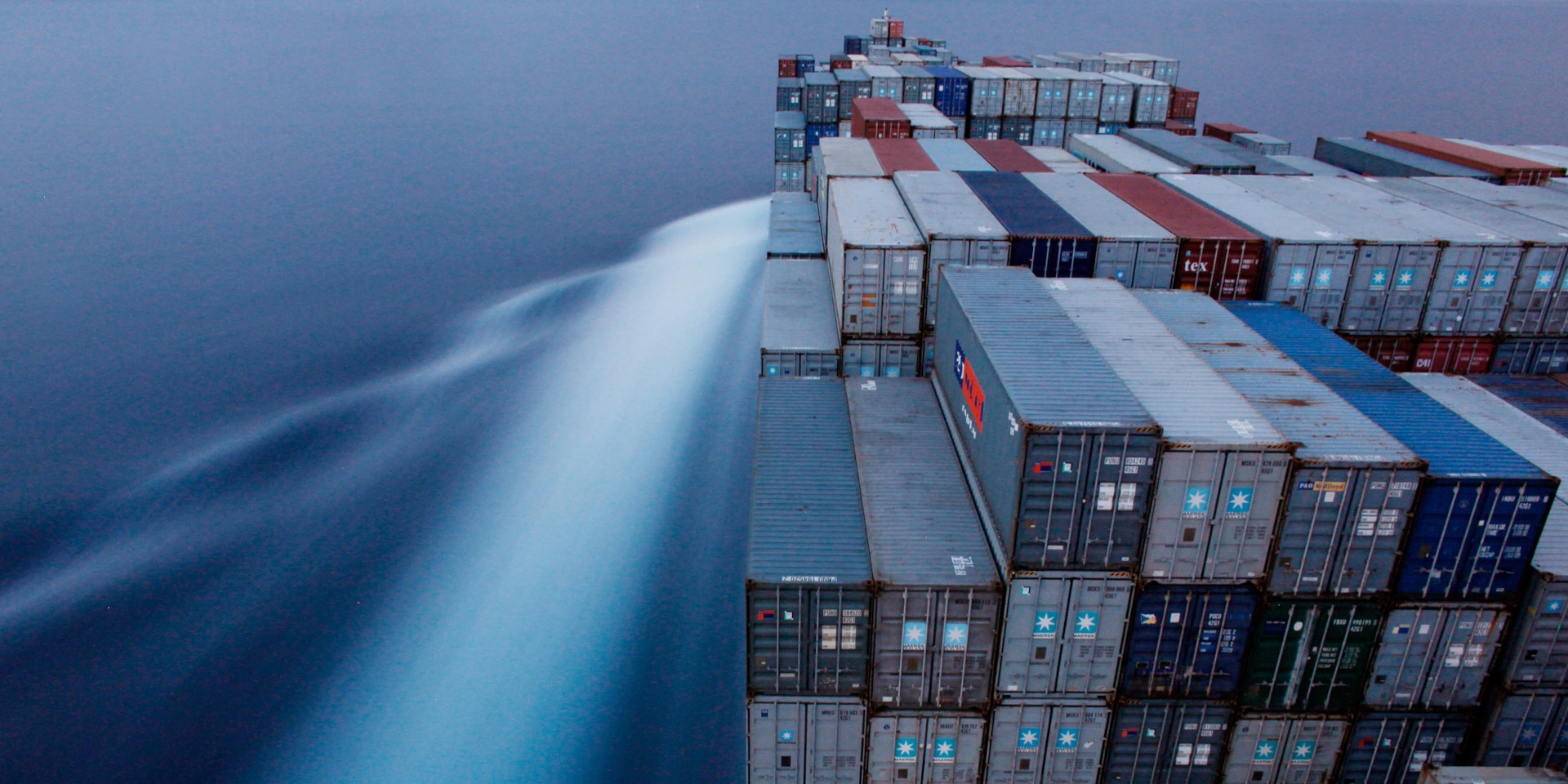 Ein Frachter transportiert zahlreiche Container. Im Hintergrund, Wasser.