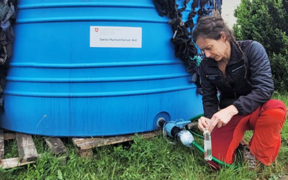 Une femme est agenouillée à côté d’un réservoir d’eau bleu et fait couler de l’eau dans une bouteille.