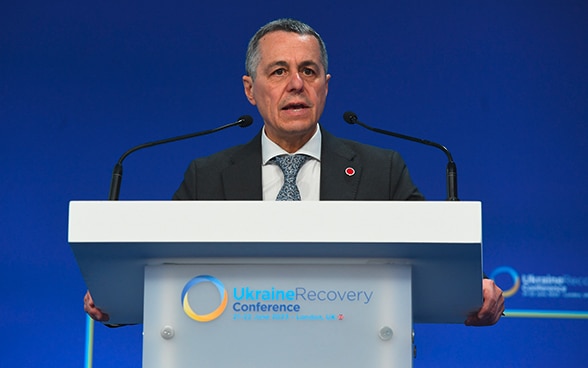 Federal Councillor Ignazio Cassis stands at a lectern and speaks. The logo of the Ukraine Recovery Conference 2023 can be seen on the front of the lectern.