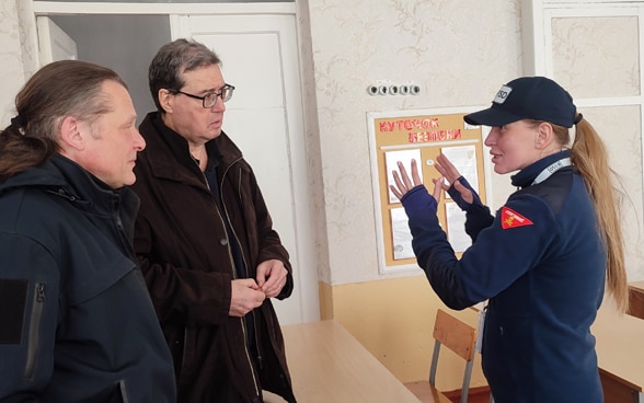 Une forme portant l’uniforme de la FSD explique quelque chose à des hommes, qui écoutent attentivement.