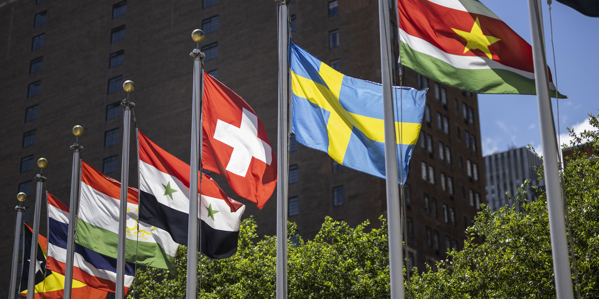 Die Schweizer Flagge, weht vor dem Hauptsitz der Vereinten Nationen neben anderen Fahnen im Wind.