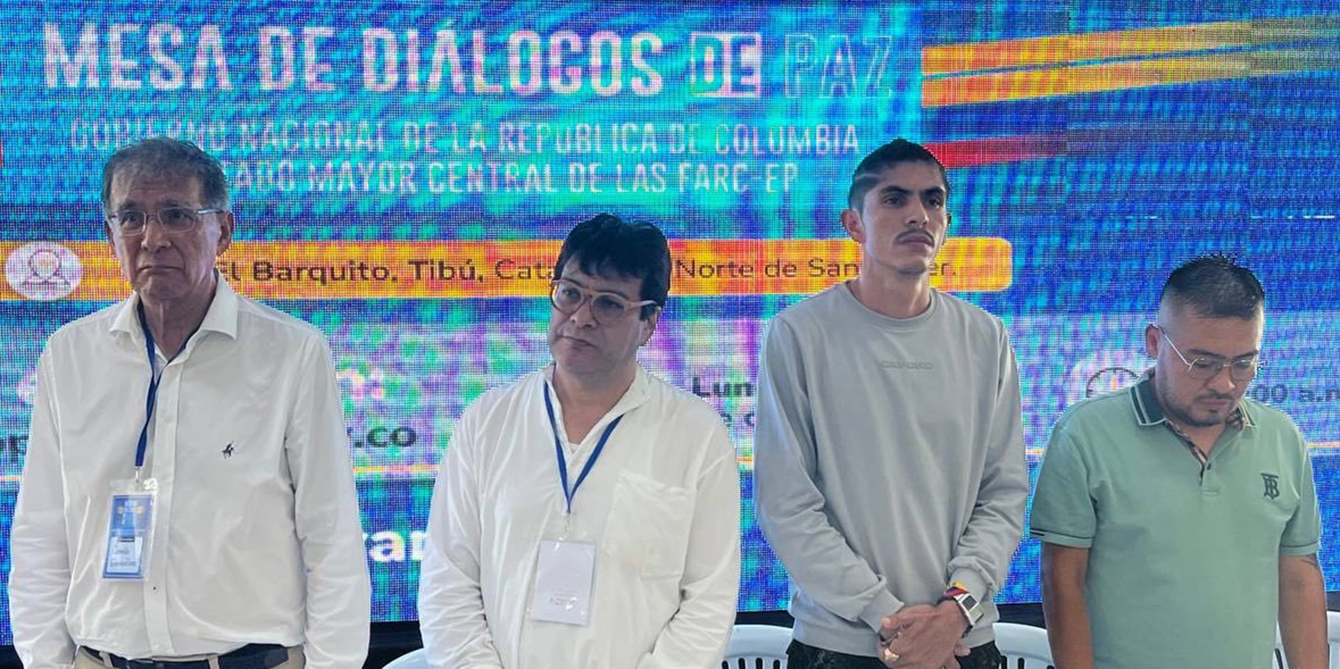 Vier ernst dreinschauende Männer stehen vor einer Rückwand mit dem Logo des Friedensdialogs.