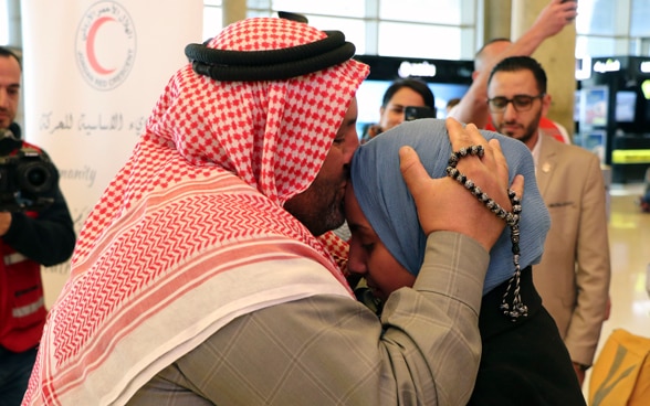 A man with a keffiyeh on his head kisses his daughter on the forehead.