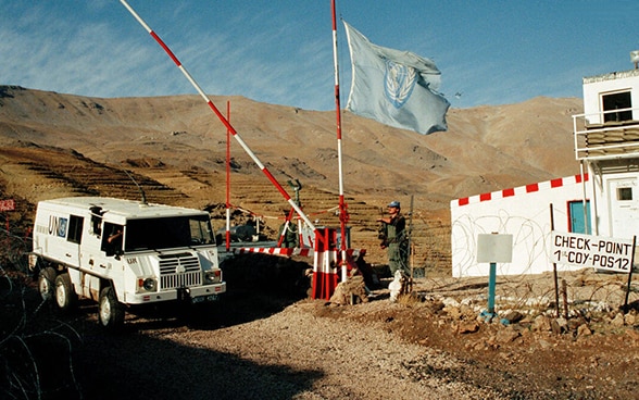 A white UN vehicle passes a checkpoint in a barren, hilly landscape.