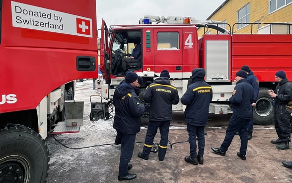 Männer des ukrainischen Zivilschutzes werden über den Gebrauch von Feuerwehrfahrzeugen, die von der Schweiz gespendet wurden, instruiert.