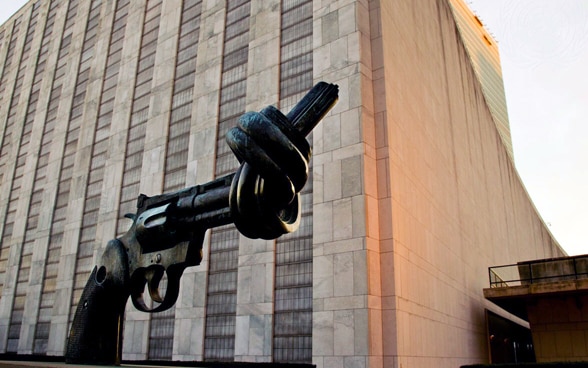 An iron sculpture in the shape of a gun with a knotted barrel stands in front of the UN headquarters in New York.