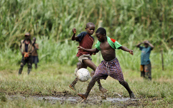 Bambini congolesi giocano a calcio su un prato in una zona rurale.