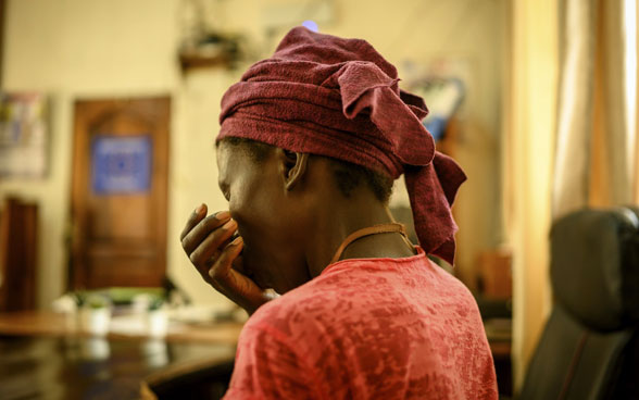 Eine Frau afrikanischer Herkunft fotografiert von hinten hält sich die Hand vor den Mund.