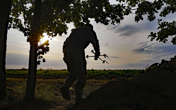 Un homme porte un drone sur la pente d’une petite colline.