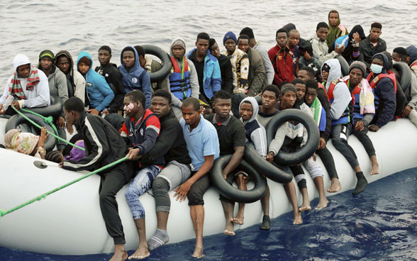 African men and women sit tightly packed in a rubber dinghy at sea.