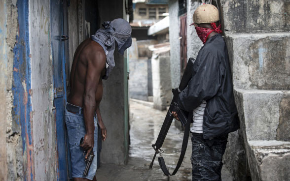 Two gang members stand armed with a revolver and a rifle in a narrow alley in Port-au-Prince, the capital of Haiti.