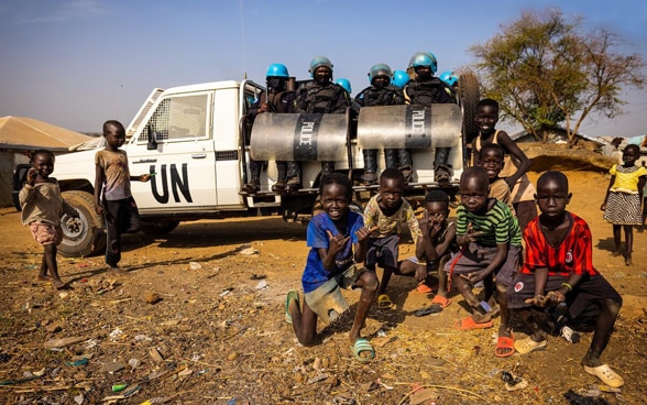 Acht UNO-Polizisten sitzen auf der Ladefläche eines weissen Pick-Ups. Im Vordergrund posieren afrikanische Kinder für das Foto.