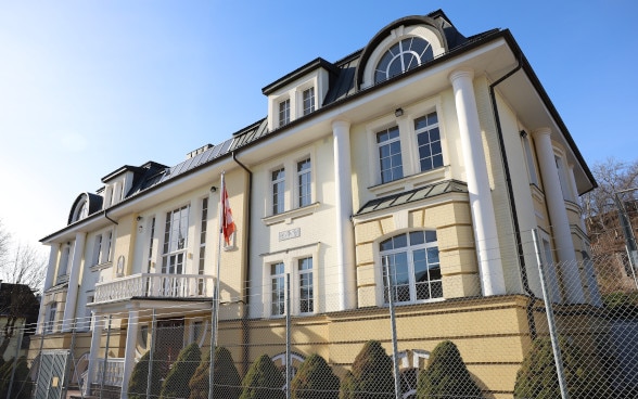 Une maison à la façade peinte en jaune clair, devant laquelle se trouve un drapeau suisse.