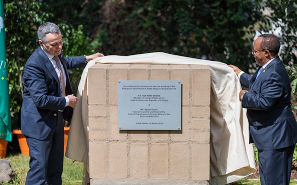 Ignazio Cassis and Taye Atske Selassie remove a sheet from a stone on which a metal plaque is affixed