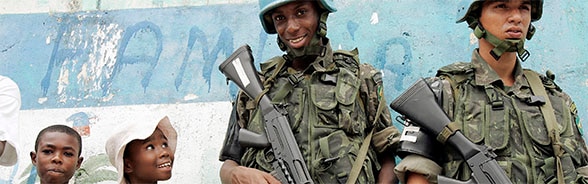 Two members of a UN armed contingent with their weapons stand next to smiling children at a demonstration of local people in Haiti