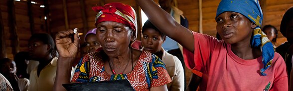 Deux femmes de la région des Grands Lacs. L’une regarde un document, l’autre lève la main.