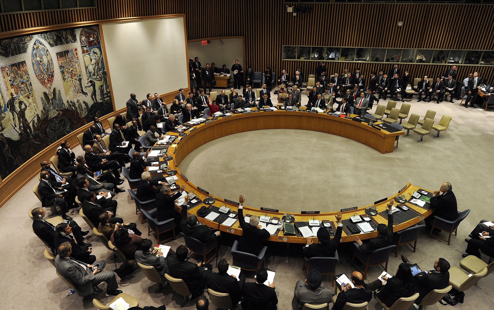 Picture of the UN Security Council: Men and women sitting in a semicircle voting on something.