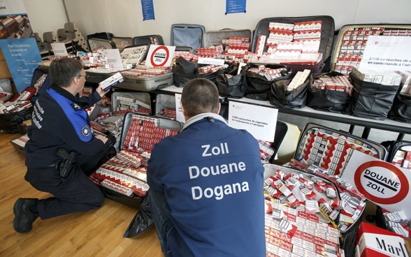 A border guard and a customs officer present 3500 cartons of cigarettes after a customs seizure at Geneva airport.