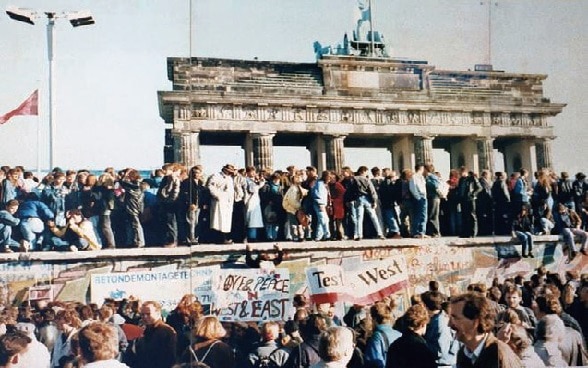 Hundreds of people from West and East Berlin standing on the wall near Brandenburg Gate.