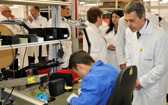 Le conseiller fédéral Ignazio Cassis observe une jeune apprentie d’un projet de formation professionnelle pendant son travail.