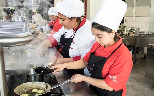 Dans une grande cuisine, des femmes sont concentrées sur les mets qu’elles préparent.